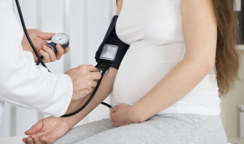 Close-up Of Male Doctor Measuring Blood Pressure Of Pregnant Woman In Clinic